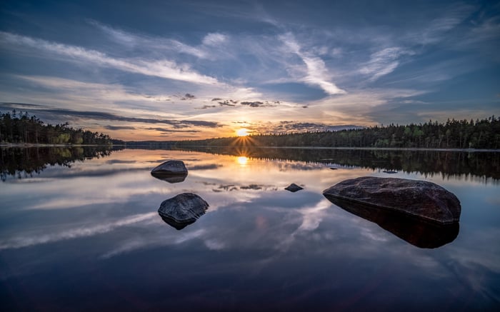 Sunset over a calm lake with rocks and forest