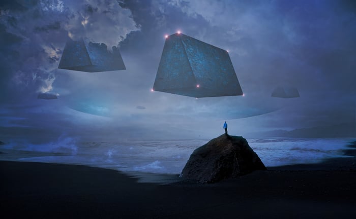 Alien pyramid ships hover over a beach with a lone figure