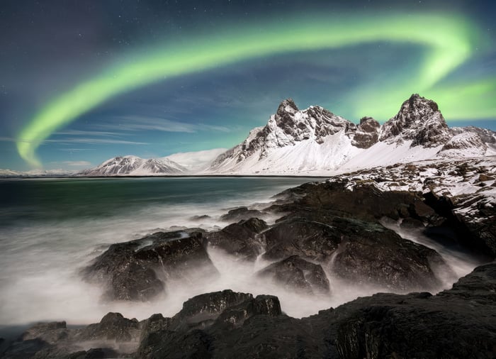 Aurora Borealis over snowy mountains and rocky coast