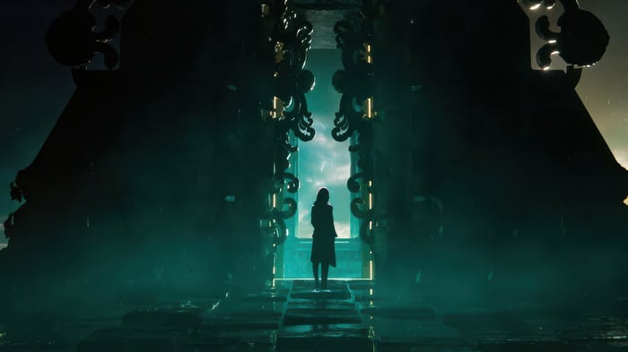 A lone figure stands before a colossal, ornate doorway.