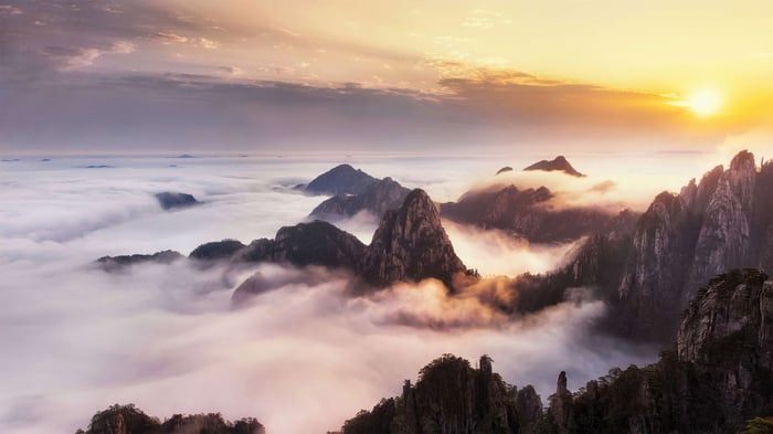 Mountain peaks emerge from sea of clouds at sunrise