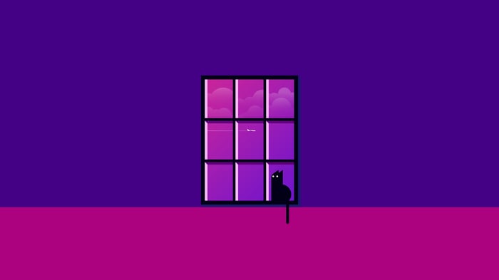A black cat sits on a windowsill at dusk.