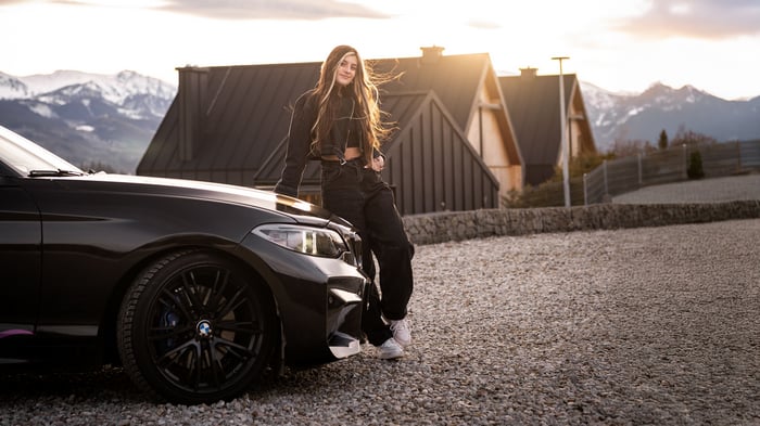 Girl leaning on a black BMW M car with mountains in the background