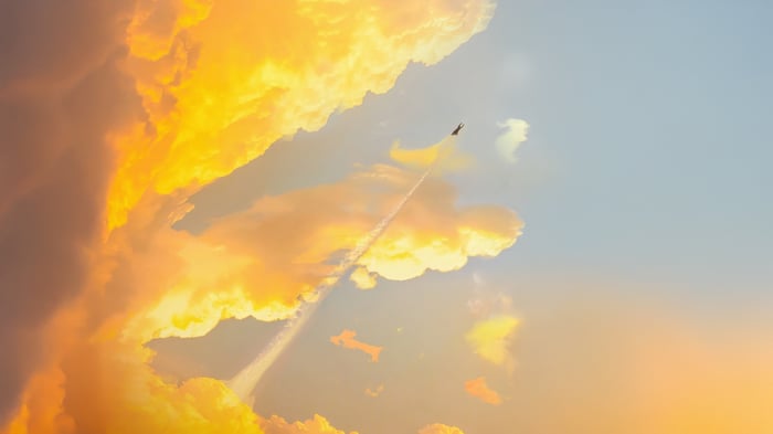 Superman flies through a sky with orange clouds