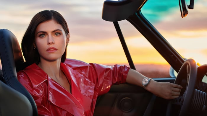 Alexandra Daddario in a red coat driving a car