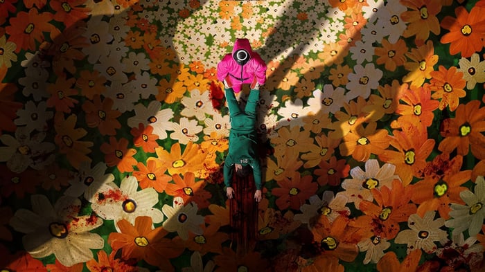 Squid Game character in pink costume and fallen player