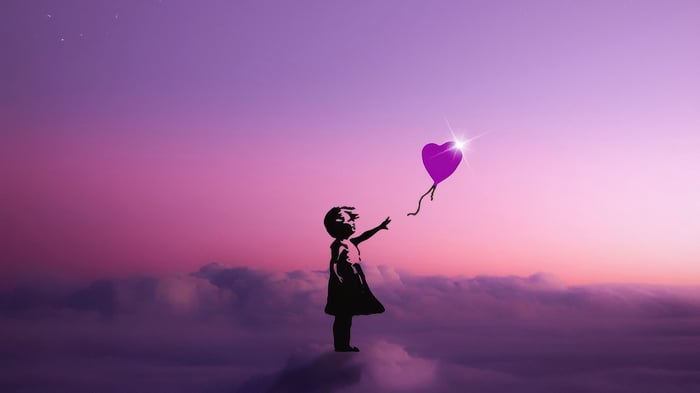 Girl reaching for a heart-shaped balloon in the sky
