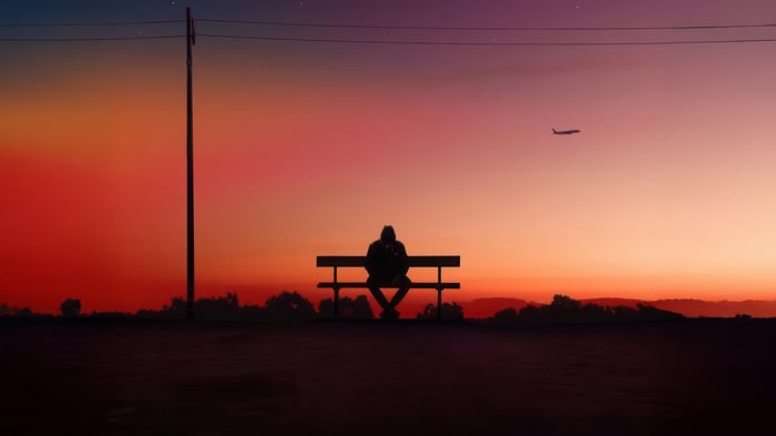 Man Sitting on Bench at Dusk with Airplane