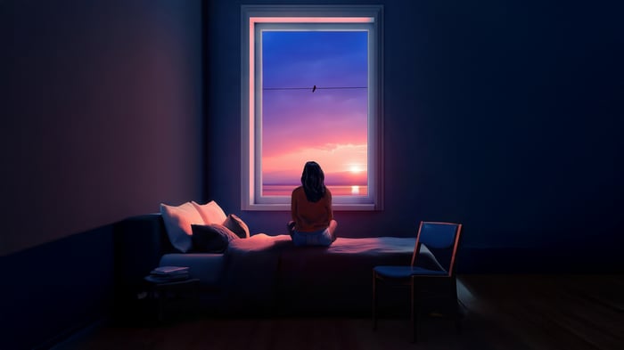 Girl sitting on bed looking out window at sunset