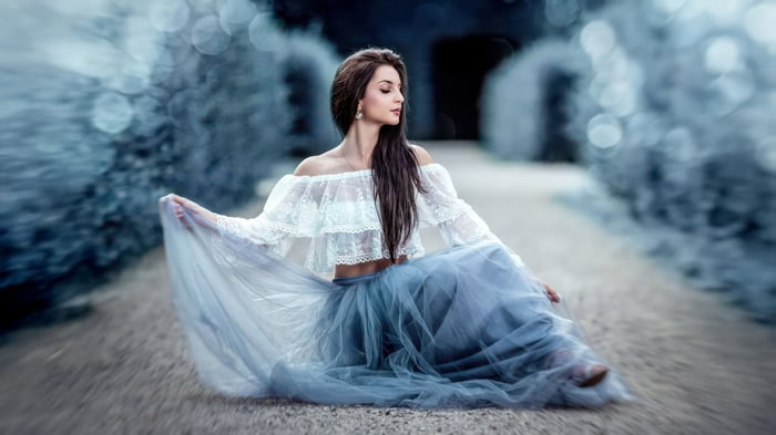 Woman in white top and blue skirt sitting on path