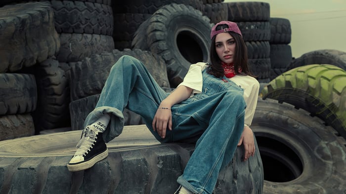 Girl in denim overalls sitting at a tire yard