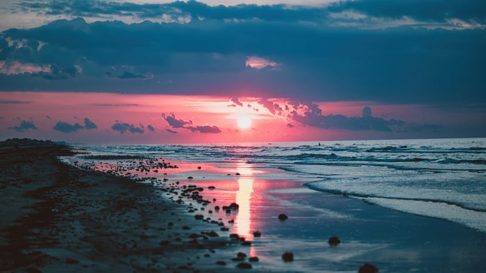 Sunset over the ocean with a beach in the foreground, 4K