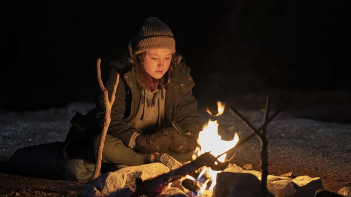 Ellie from The Last of Us sits by a campfire