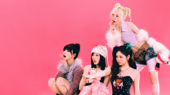 Aespa members in colorful outfits on pink background