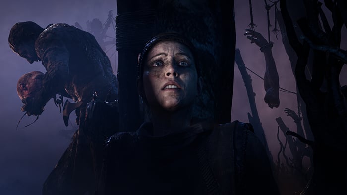A woman looks up in horror at monstrous figures and hanging bodies