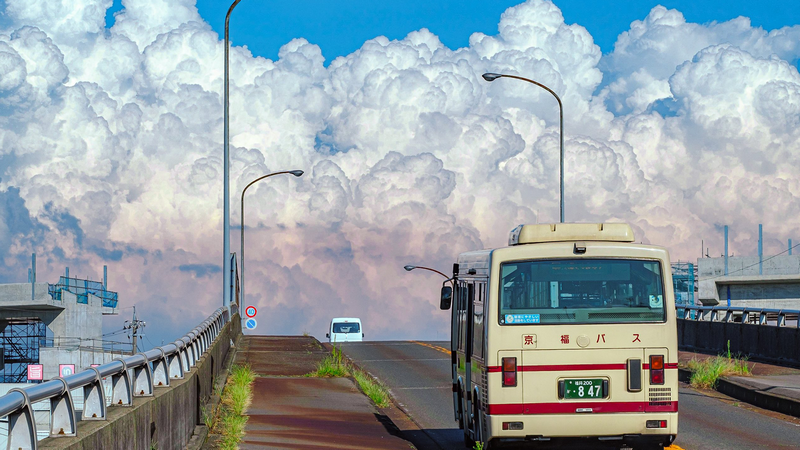 A bus drives up a road under a cloudy sky