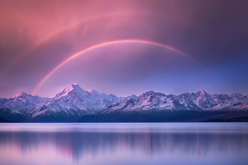Rainbow over snow-capped mountains reflected in a lake
