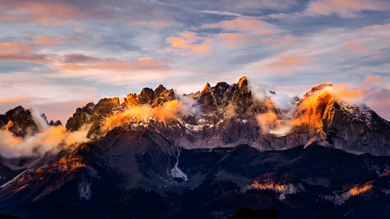 Snow-capped mountains bathed in golden sunlight with clouds