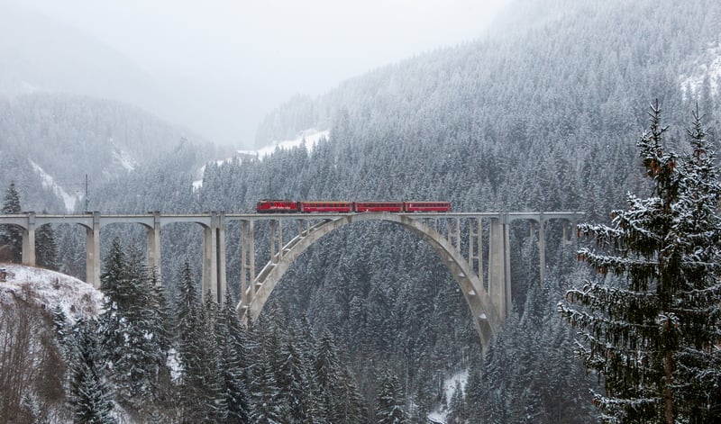 Red train crossing a snowy viaduct bridge in a winter forest