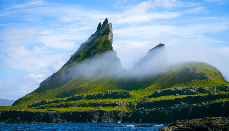 Misty green peaks rise from the ocean near rocky shores