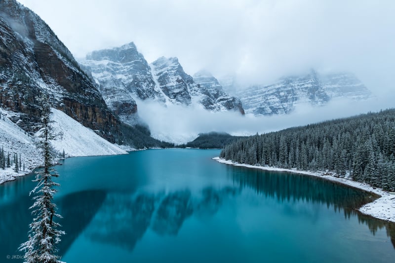 Snowy mountains and pine forest reflected in a turquoise lake