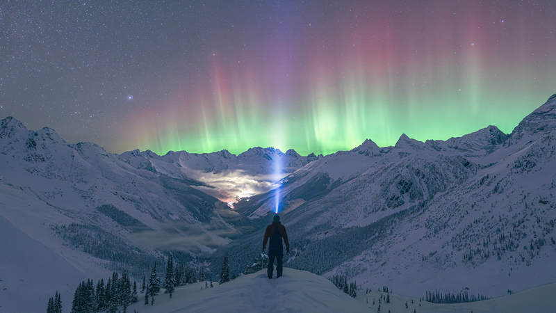 Man watches Aurora Borealis over Selkirk Mountains, Canada
