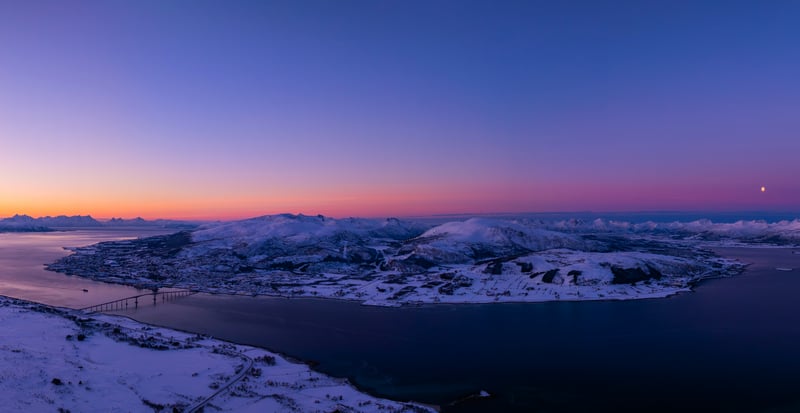 Snowy landscape with a bridge over water at sunset