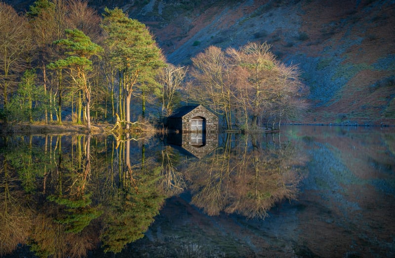 Stone boathouse reflected in a calm lake with trees