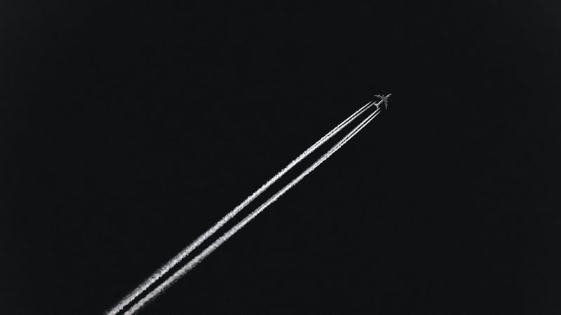 Passenger aircraft leaving contrails against a dark sky
