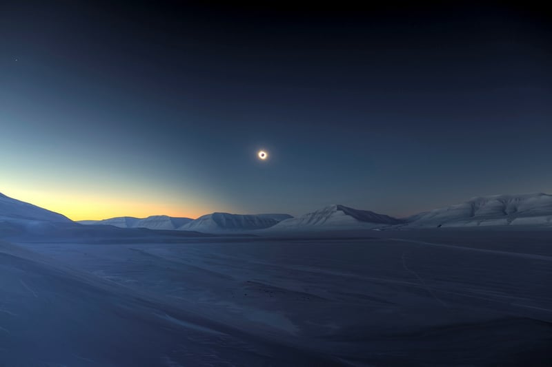 Solar eclipse over snow-covered mountains at twilight