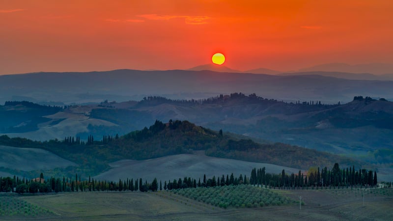 Sunset over rolling hills and cypress trees in Tuscany
