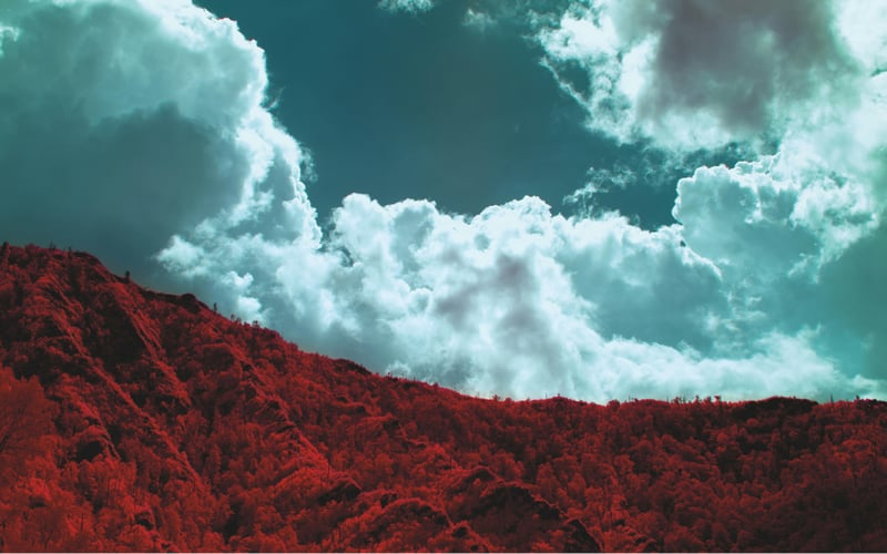Surreal infrared landscape with red mountains and blue clouds