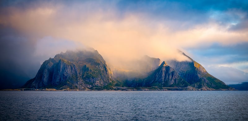 Misty mountains rise from the sea under cloudy sky