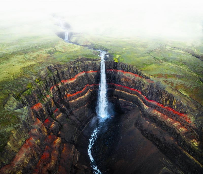 Aerial view of a waterfall cascading over colorful cliffs in Iceland