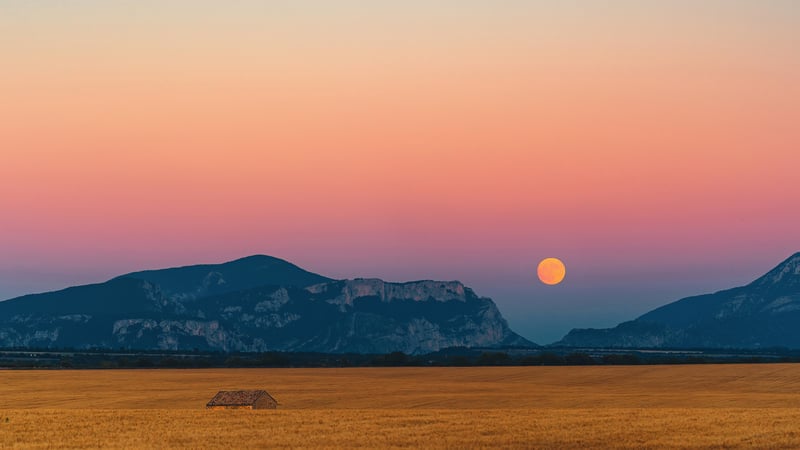 Sunset over mountains with a full moon and field