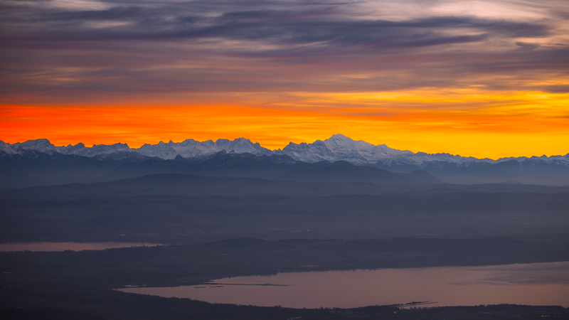 Aerial view of snowy mountain peaks over a lake at sunset