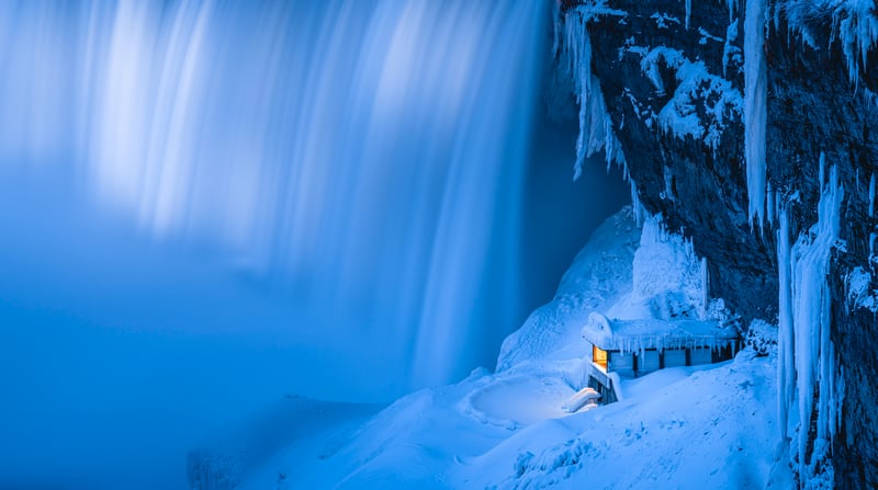 Frozen waterfall with a small illuminated cabin in winter