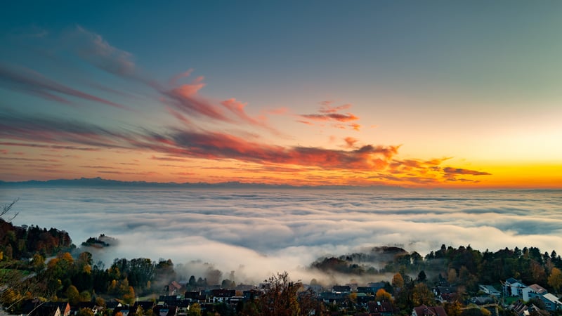 Village nestled in fog below a colorful sunset sky