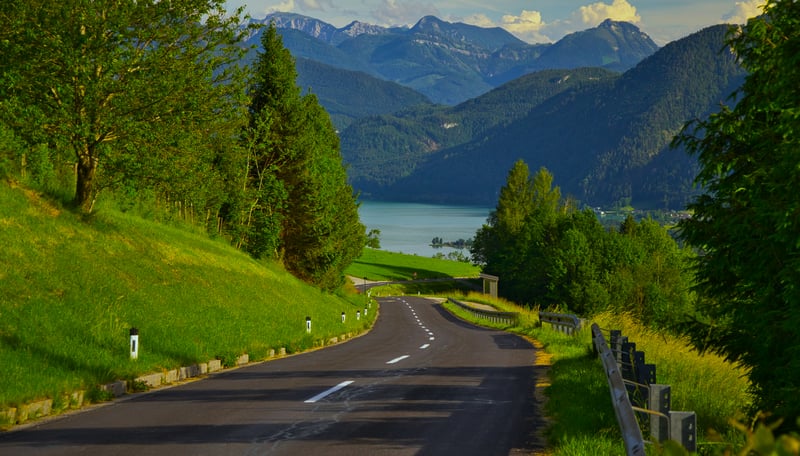 Winding road through green hills towards a lake and mountains