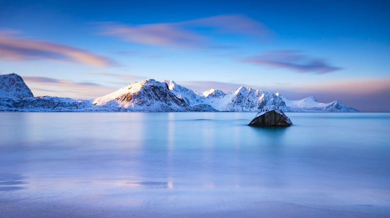 Snow-capped mountains reflected in calm water with a rock