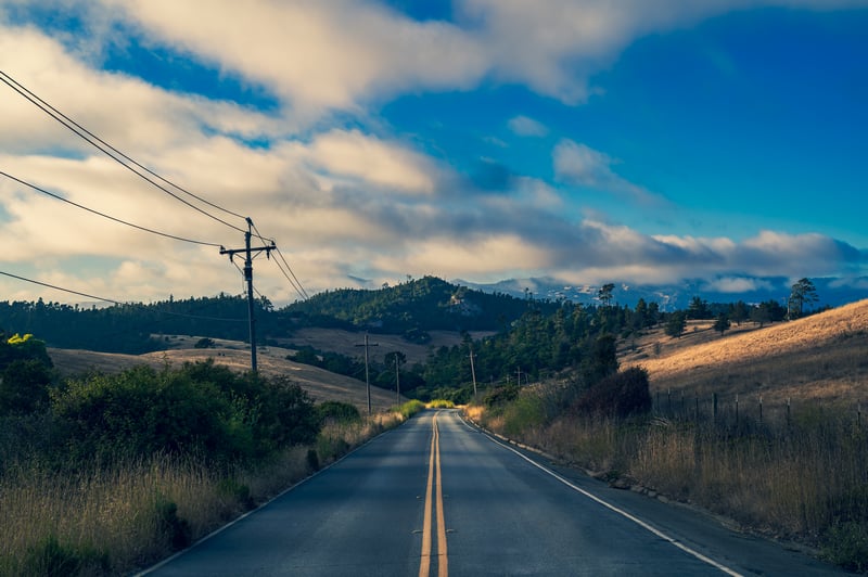 Road through California hills with mountains and clouds