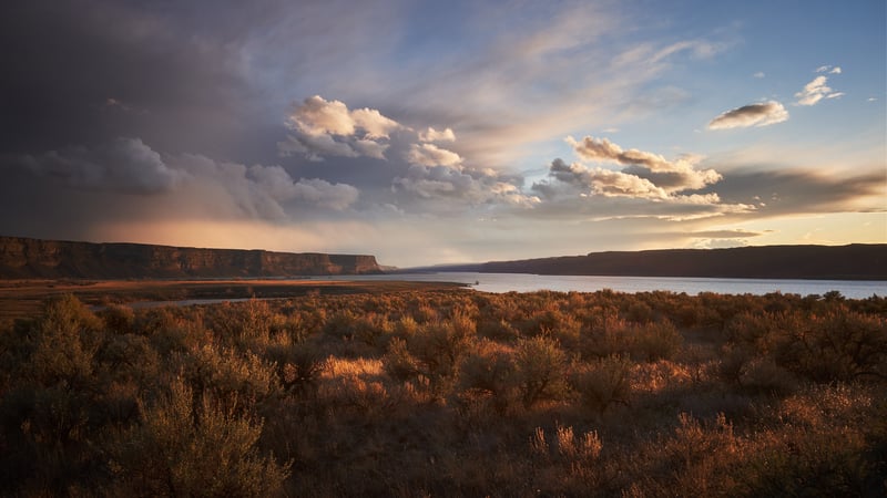 Sunset over a wide river with clouds and dry brush
