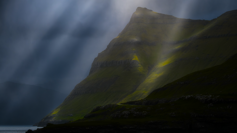 Sun rays over Faroe Islands mountains and water