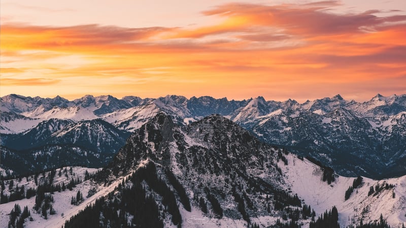 Snow-covered mountains under orange sunset sky