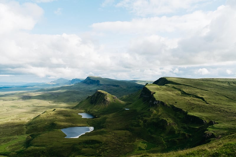 Green rolling hills with small lakes under cloudy sky