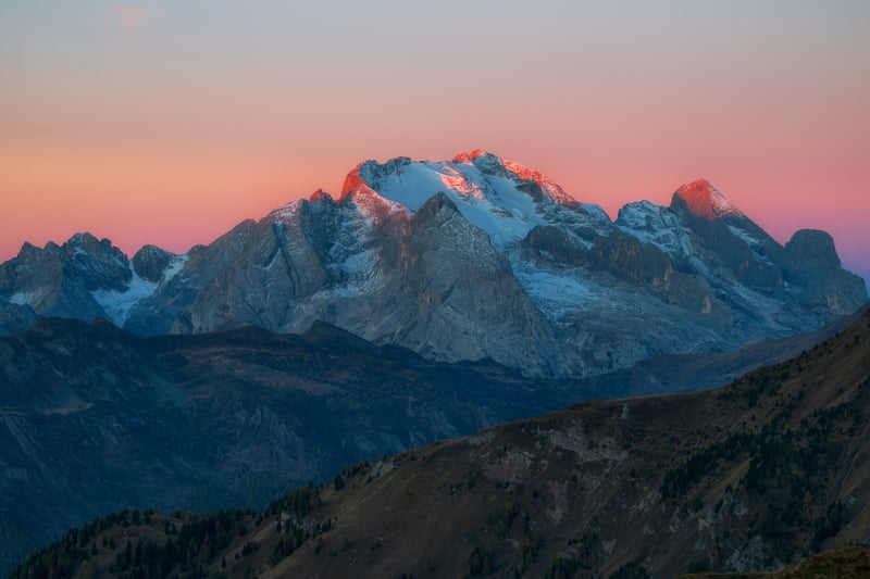 Snow-capped mountain range at sunrise with pastel sky