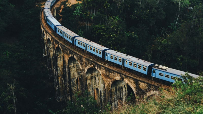 Blue train crossing a historic nine-arch railway bridge in Sri Lanka