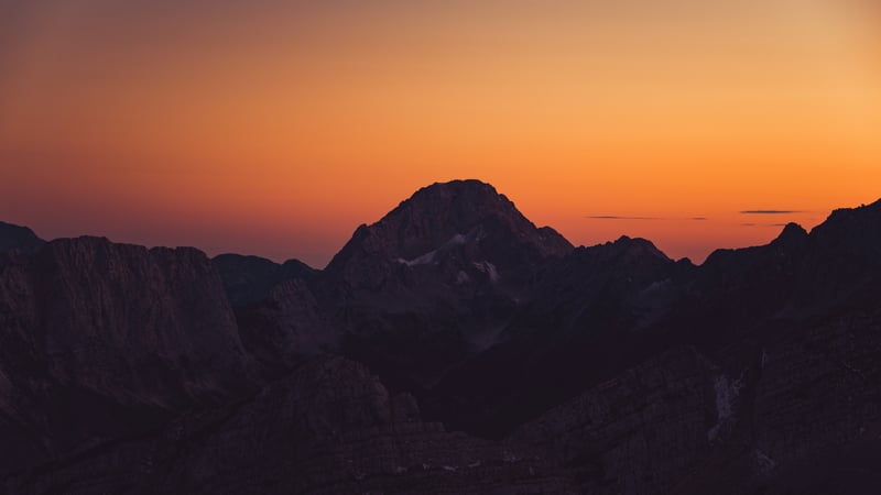 Silhouette of mountains against an orange sunset sky