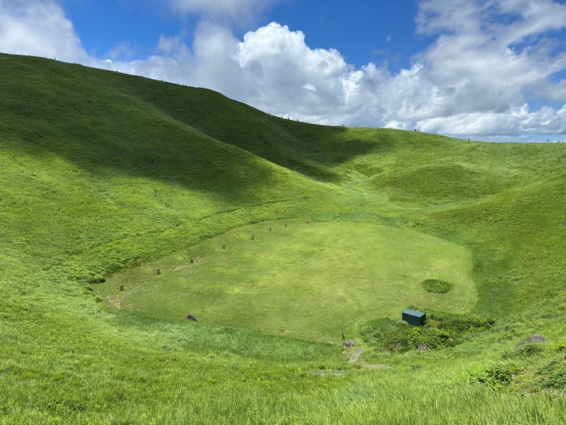 Green grassy crater with a small shelter under a cloudy sky