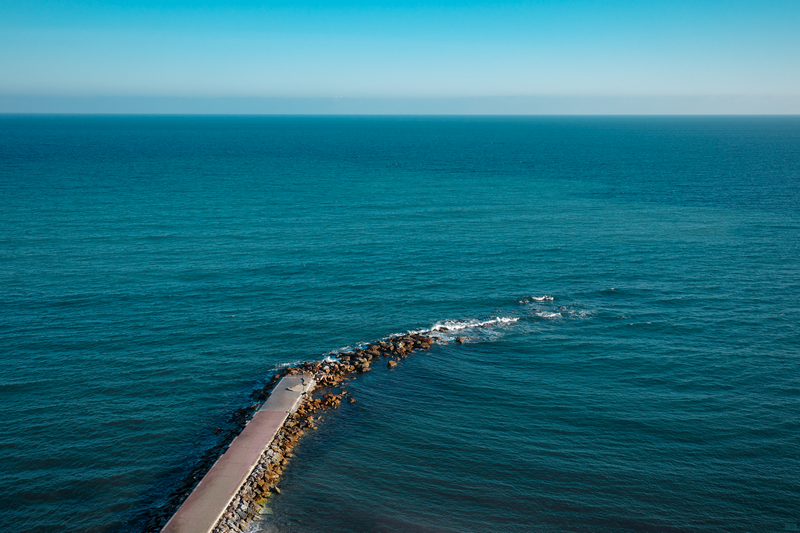 Stone pier extending into the vast blue sea under a clear sky